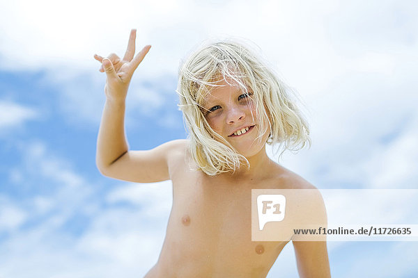 Junge (8-9) zeigt Friedenszeichen vor blauem Himmel