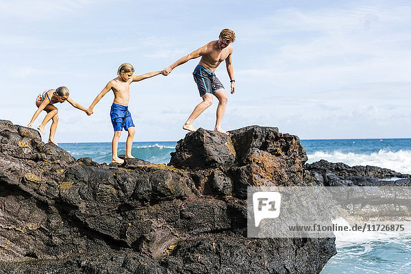 Mann und Kinder (6-7  8-9) gehen auf einem Felsen am Meer