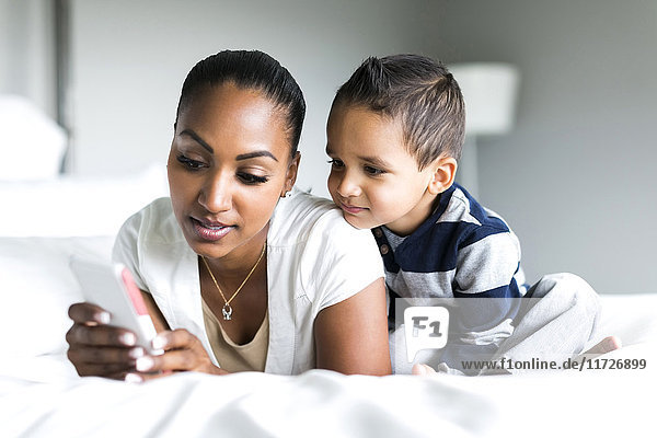 Mutter und Sohn (2-3) liegen auf dem Bett und benutzen ein Smartphone