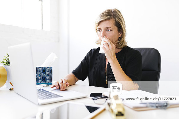 Frau benutzt Laptop  schnäuzt sich die Nase