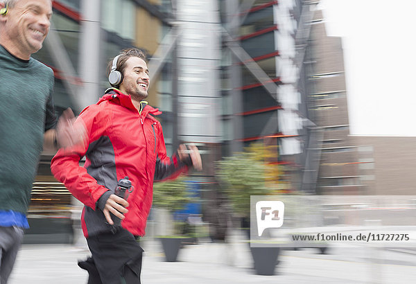 Smiling men running  wearing headphones on urban sidewalk