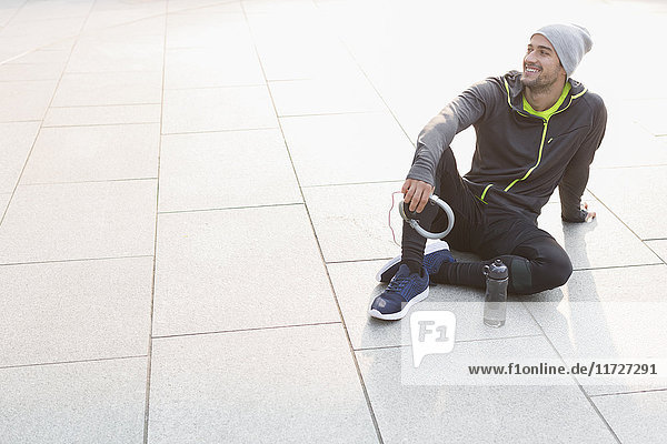 Smiling male runner resting  holding headphones and looking away