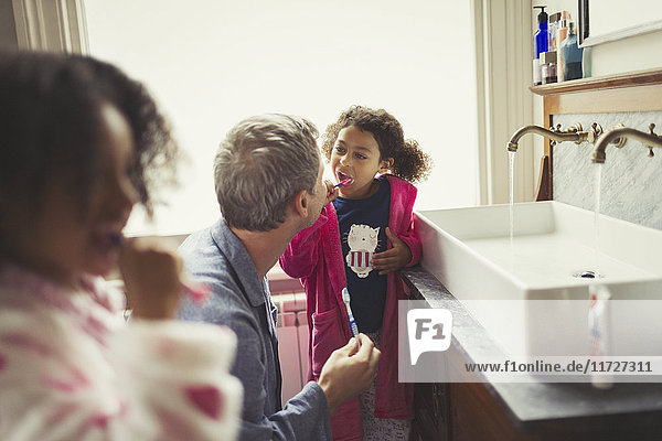 Ein multiethnischer Vater beobachtet die Tochter beim Zähneputzen am Waschbecken.