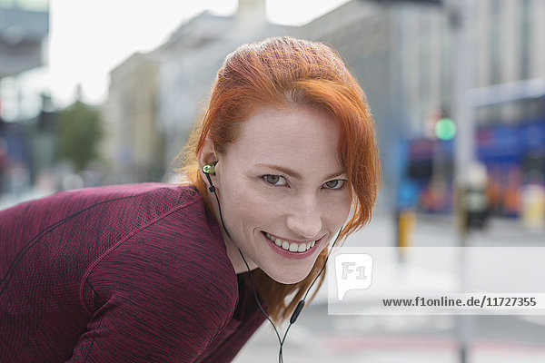 Porträt einer lächelnden Läuferin mit Kopfhörern  die auf einem städtischen Bürgersteig ruhen