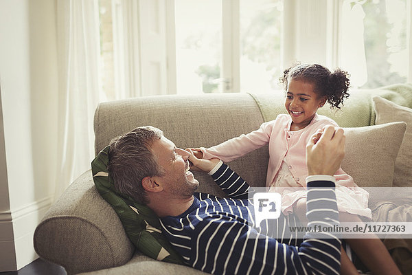 Affectionate multi-ethnic father and daughter holding hands on sofa