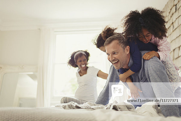 Multi-ethnic daughters tackling father on bed