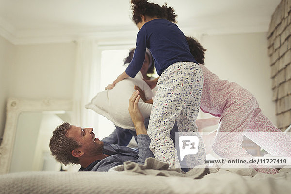 Verspielte multi-ethische Vater- und Töchter-Kissenschlacht auf dem Bett