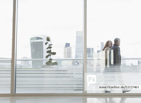 Geschäftsmann und Geschäftsfrau zu Fuß auf dem städtischen Hochhausbalkon mit Blick auf die Stadt