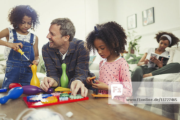 Multi-ethnischer Vater und Töchter beim Spielen mit Spielzeug im Wohnzimmer