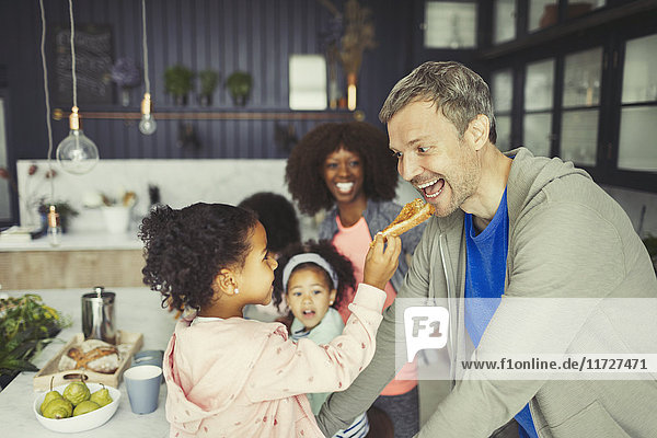 Multi-ethnic daughter feeding toast to father in kitchen