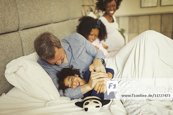 Multi-ethnischer Vater und Tochter kitzeln und lachen auf dem Bett