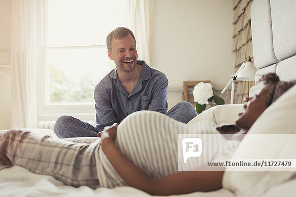Multi-ethnic pregnant couple relaxing and laughing on bed