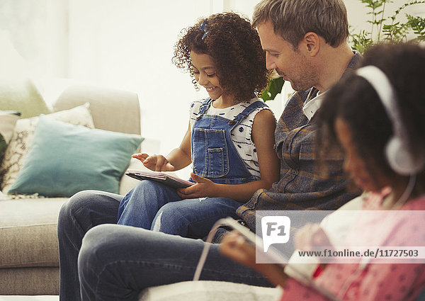 Multi-ethnischer Vater und Tochter mit digitalem Tablett auf Sofa