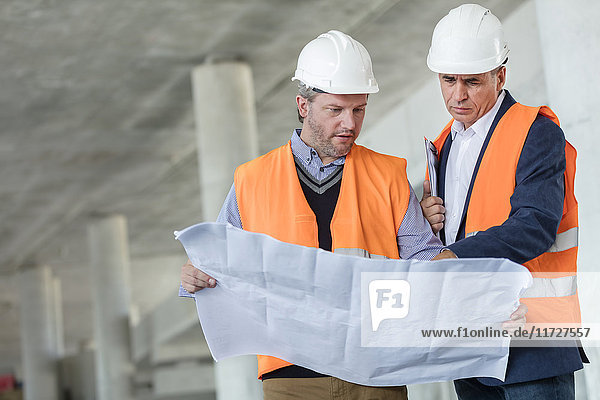 Male engineers examining underground blueprints at construction site