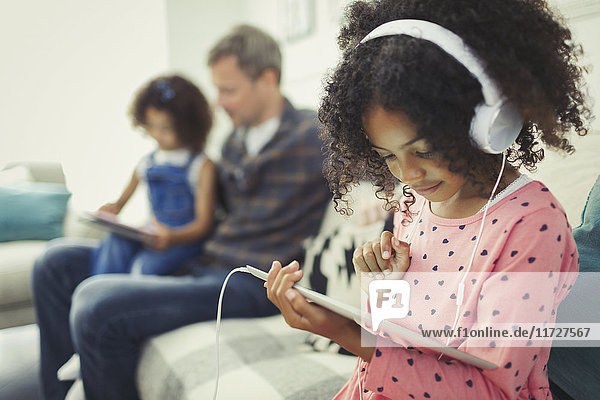 Mädchen mit Kopfhörer mit digitalem Tablett auf dem Sofa