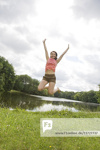Pretty young woman jumping by a lake