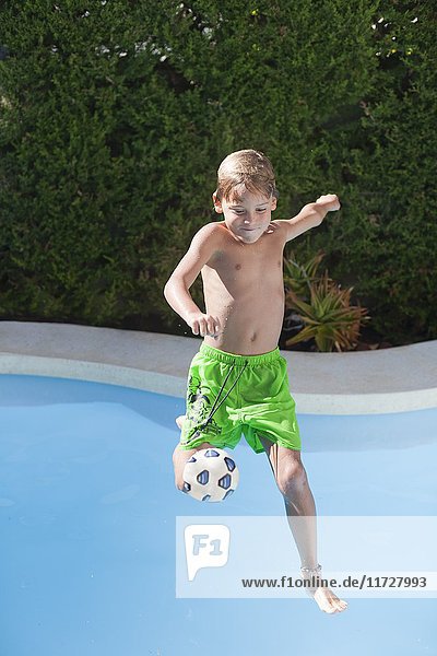 Kleiner Junge  der in den Pool springt und den Ball tritt.