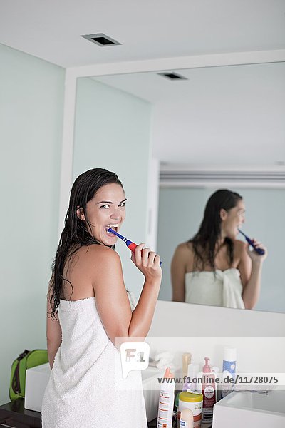 Brunette woman brushing her teeth in front of the mirror