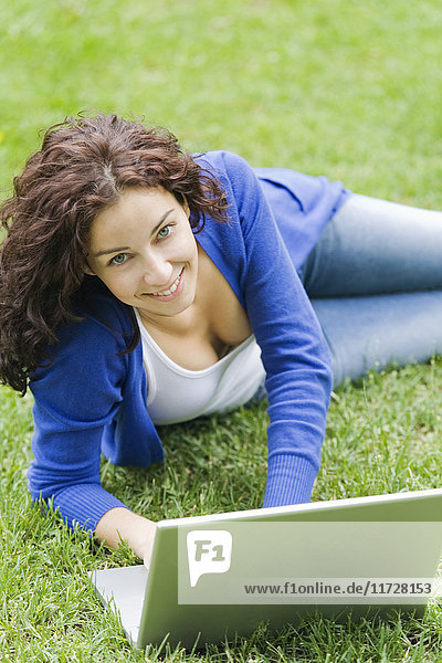 Zufriedene Frau mit im Park liegendem Laptop