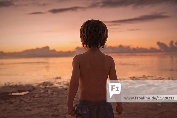 Junge am Strand mit Blick auf ruhigen Sonnenuntergang Meer