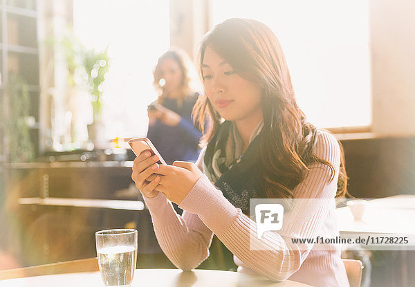 Frau  die mit ihrem Handy am Tisch eines Cafés SMS schreibt