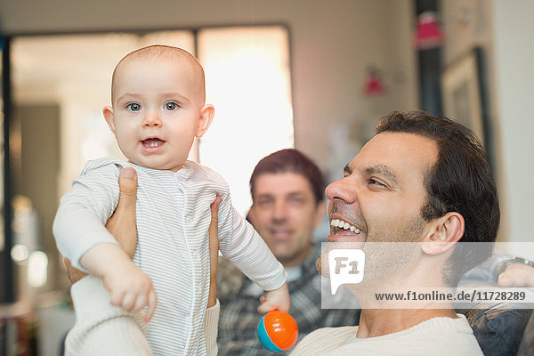 Portrait glückliche männliche schwule Eltern halten Baby Sohn im Wohnzimmer