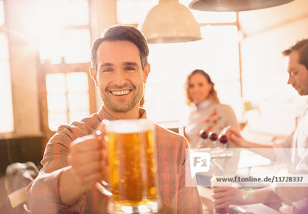 Porträt eines lächelnden Mannes  der in einer Bar auf einen Bierkrug anstößt