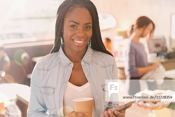 Porträt einer lächelnden afrikanischen Frau  die ein Mobiltelefon benutzt und Kaffee in einem Café trinkt