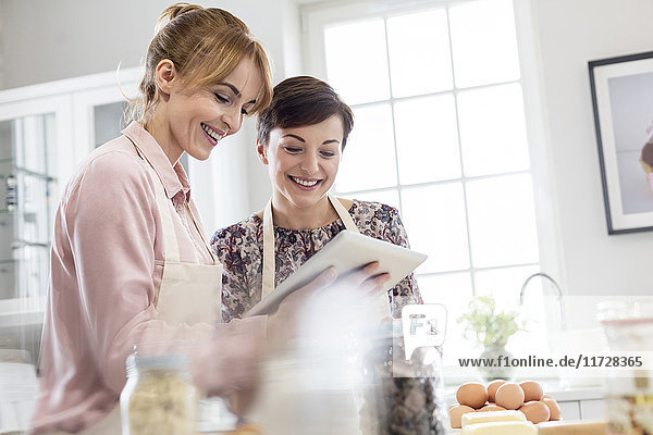 Smiling female caterers using digital tablet  baking in kitchen