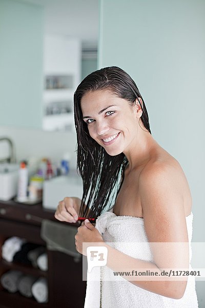 Brünette Frau bürstet sich die Haare und lächelt in die Kamera.