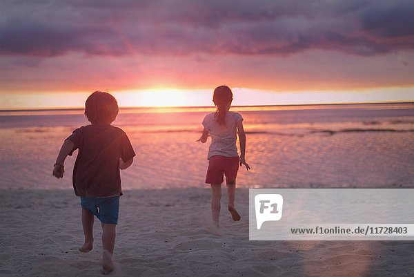 Junge und Mädchen Bruder und Schwester auf ruhigen Sonnenuntergang Strand mit dramatischen Himmel