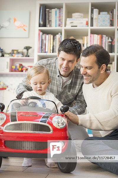 Male gay parents pushing baby son in toy car