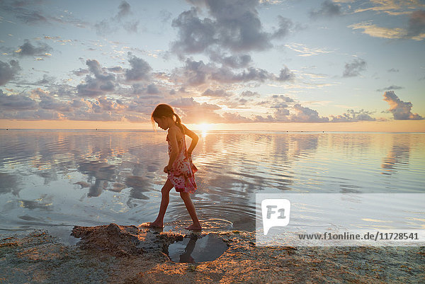 Mädchen watet in der Meeresbrandung am ruhigen Strand bei Sonnenuntergang