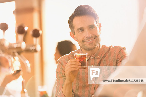 Lächelnder Mann  der an einer Bar einen Cocktail trinkt