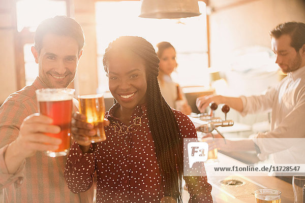 Portrait lächelndes Paar stößt mit Biergläsern an der Bar an
