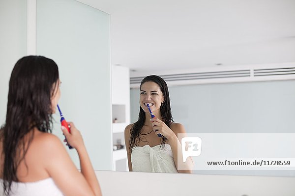 Brünette Frau beim Zähneputzen vor dem Spiegel