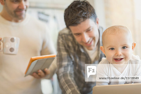 Portrait cute baby son with male gay parents using digital tablet