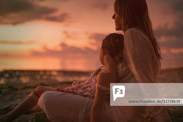 Gelassene Mutter und Tochter entspannen am Strand in der Abenddämmerung