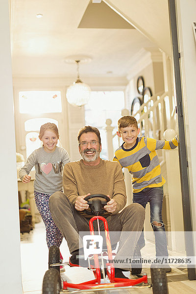 Portrait lächelnde Kinder schieben Vater auf Spielzeugauto im Foyer Flur