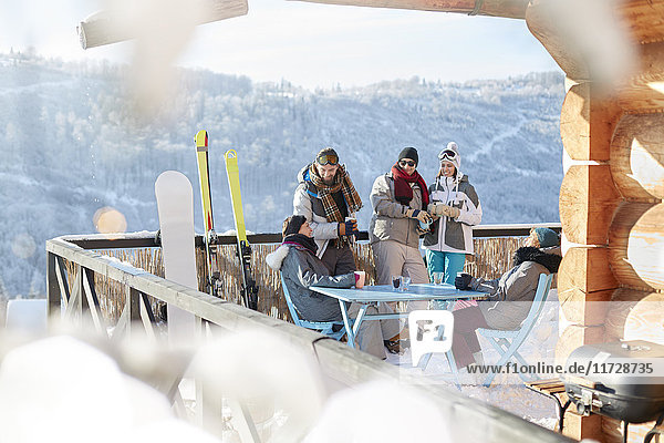 Skifahrer- und Snowboarderpaare hängen auf dem sonnigen Hüttenbalkon Apres-Ski.