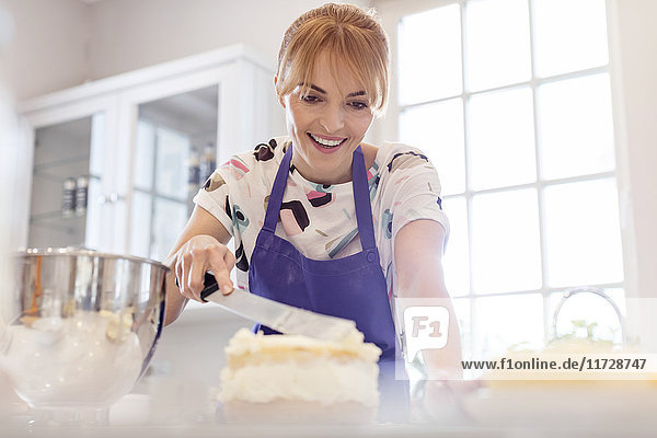 Smiling woman baking  icing layer cake in kitchen