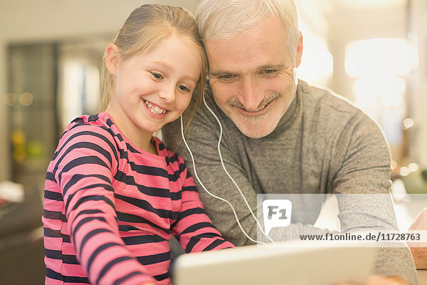 Lächelnder Vater und Tochter teilen sich Kopfhörer und sehen sich Videos auf einem digitalen Tablett an.