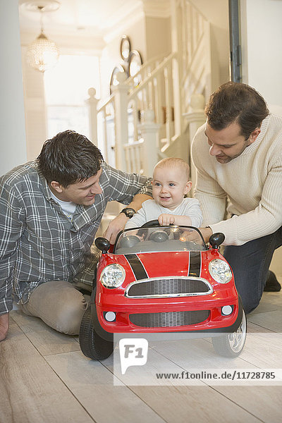 Male gay parents and baby son playing with toy car