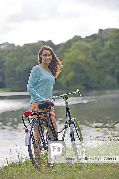 Hübsche junge Frau mit Fahrrad im Park in der Nähe eines Sees