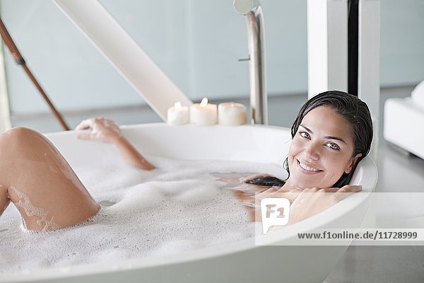 Young pretty brunette woman enjoying a bath and smiling at camera
