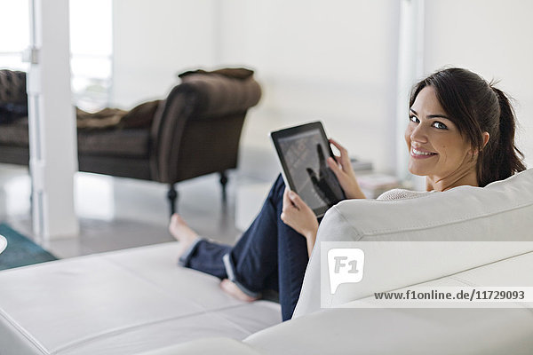 Beautiful brunette woman on a couch with tablet smiling at camera
