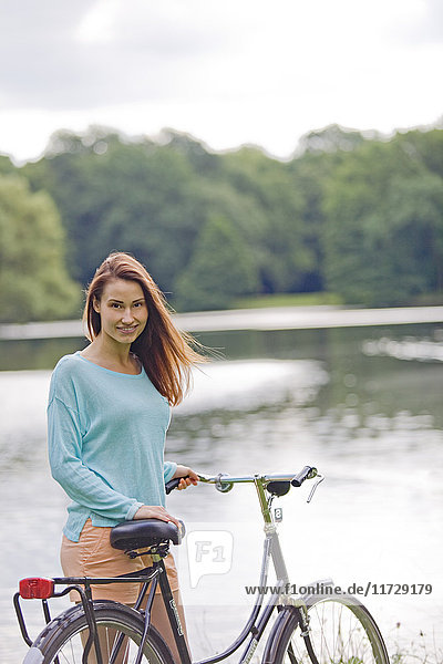 Pretty young woman with bicycle in park and lake