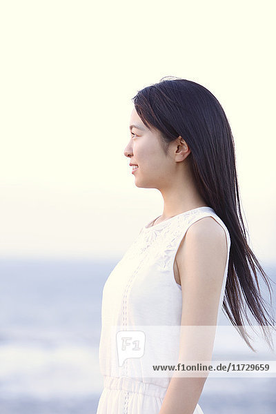 Junge Japanerin in einem weißen Kleid an einer Klippe über dem Meer bei Sonnenaufgang  Chiba  Japan