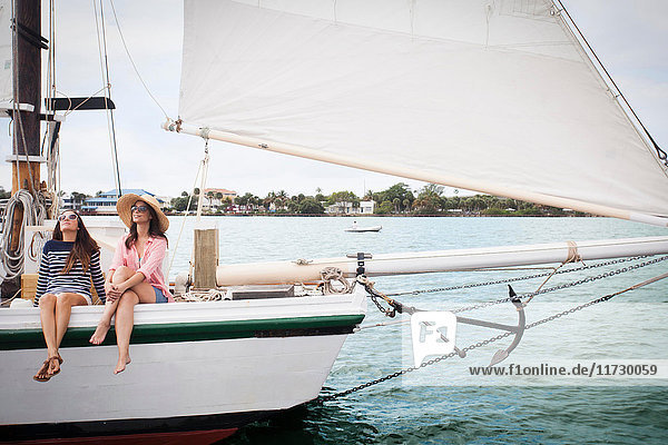 Two women on sitting on edge of sailing boat  legs dangling over the edge