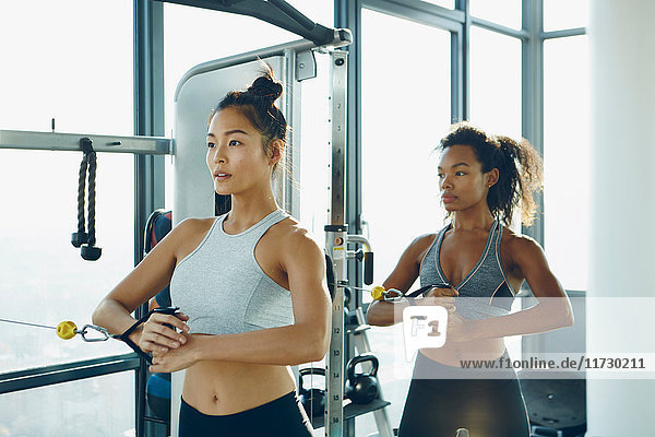 Zwei junge Frauen trainieren im Fitnessstudio und benutzen dabei Fitnessgeräte